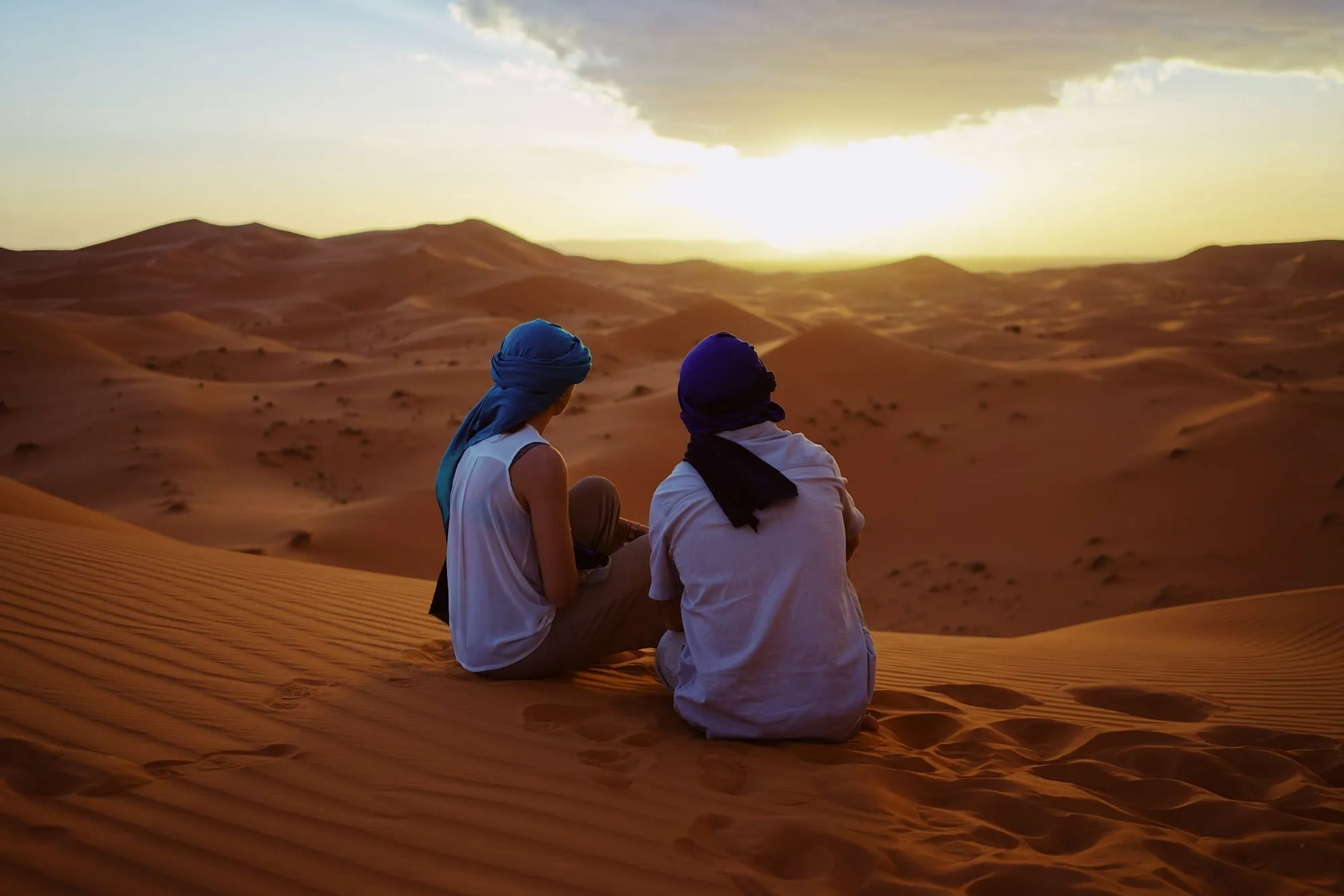 Dos viajeros contemplando el atardecer sobre las dunas del Sáhara
