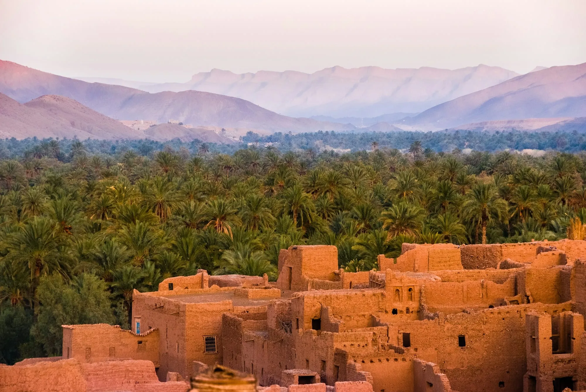 Kasbah de adobe junto a un palmeral, con las montañas del Atlas al fondo